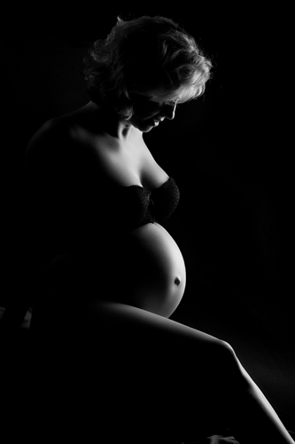 Schwangerschaftsfotografie Düsseldorf. Schwangere mit nacktem Babybauch tritt halb aus dem Dunkel. Sie sieht aus wie Marylin Monroe. Babybauchfotografin A. Ola Karlowski. Schwangerschaftsfotografie Düsseldorf.