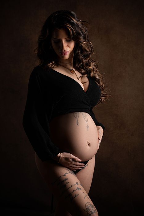 Stark. Schön. Schwanger. Babybauchfoto mit Tattoo. Schwangere Frau steht vor dunkelbraunem Hintergrund, ihren bauch haltend und Blick nach unten. verträumt. Stark. Schön. Schwanger. Babybauchfoto mit Tattoo. Schwangere Frau steht vor dunkelbraunem Hintergrund, ihren bauch haltend und Blick nach unten. verträumt.