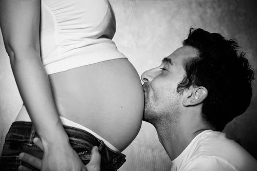 Schwarz-weiß Babybauchfotografie in Düsseldorf: Partner küsst liebevoll den Babybauch der werdenden Mutter.