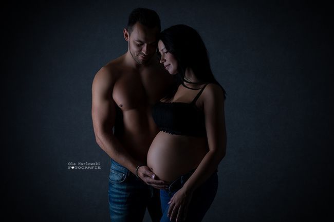 Intime Babybauchfotografie mit Partner in Düsseldorf: Paar umarmt sich im dunklen Studio-Setting.