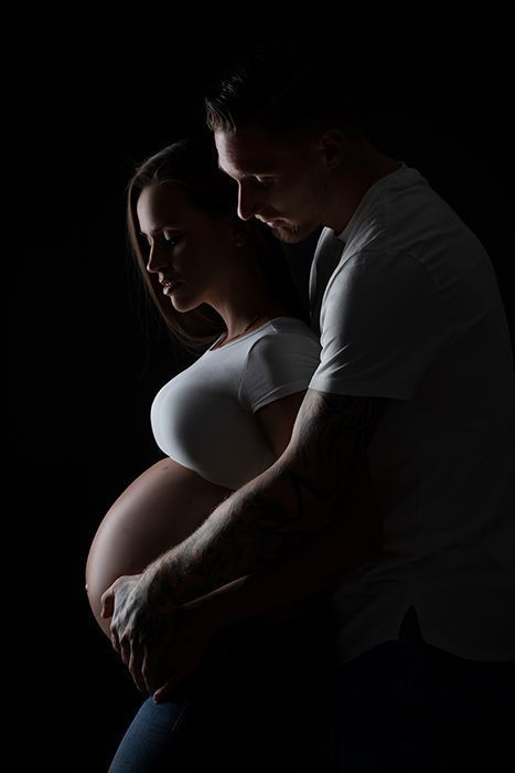 Emotionale Partner-Schwangerschaftsfotografie in Düsseldorf: Paar hält gemeinsam den Babybauch in ruhiger Studioatmosphäre.