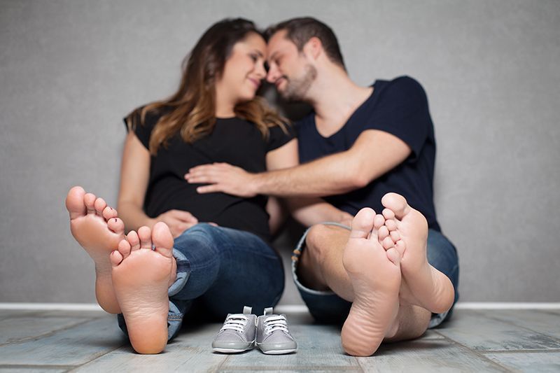 Partner-Babybauchfotografie in Düsseldorf: liebevolles Paar sitzt entspannt im Studio und hält gemeinsam den Babybauch