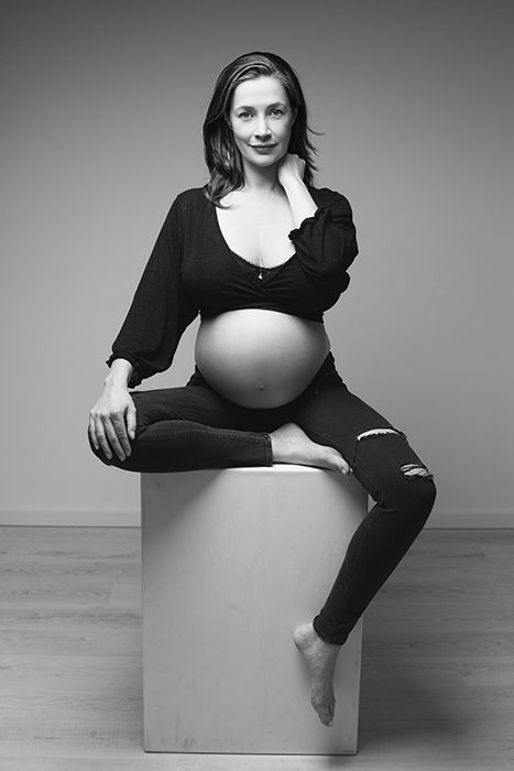 Zeitlose Schwarz-weiß Schwangerschaftsfotografie in Düsseldorf: sitzendes Studio-Portrait einer werdenden Mutter mit klarer Linienführung.